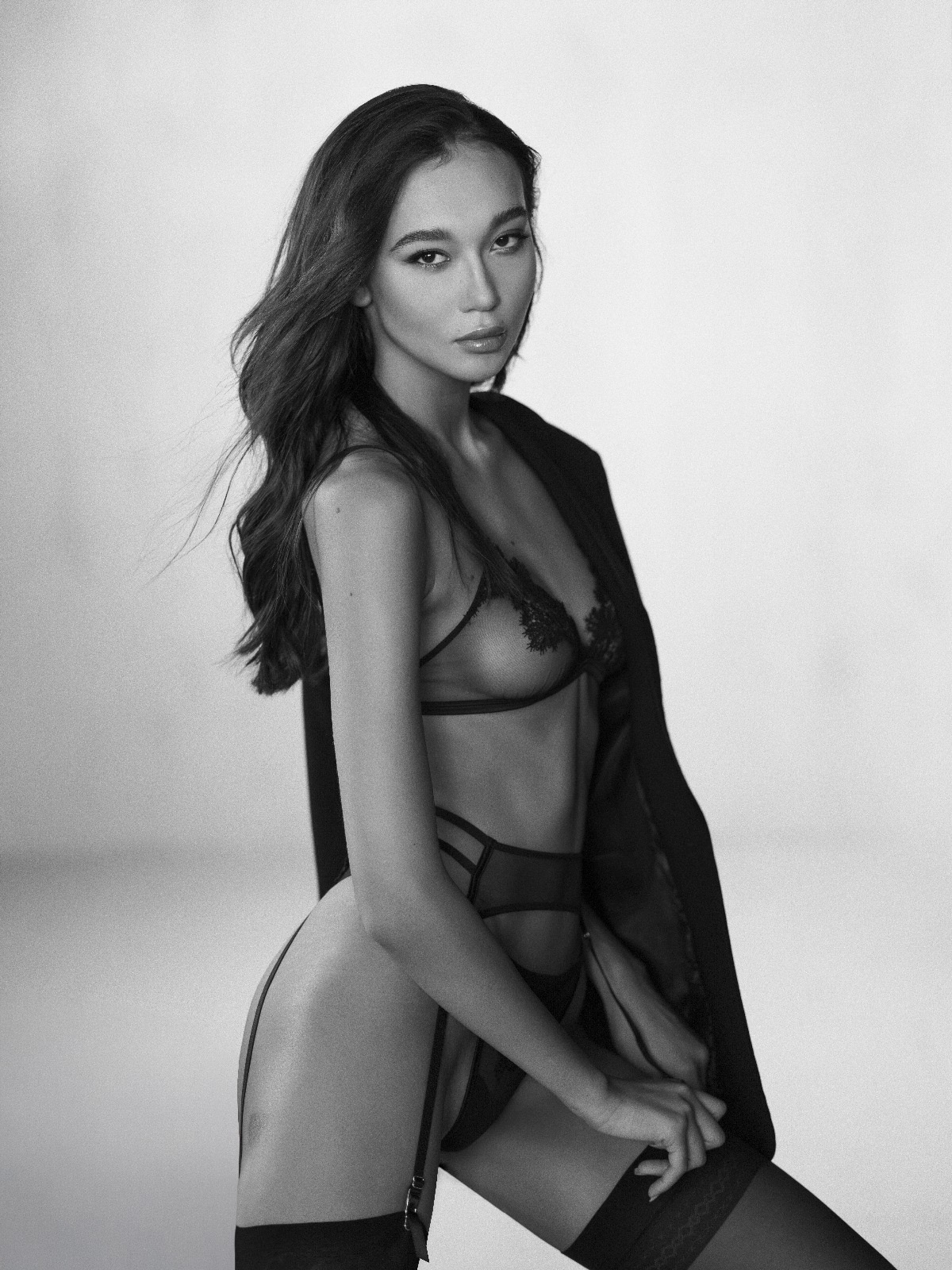 Modella elegante in lingerie nera, posa seducente con giacca, fotografia di moda artisticamente scattata.
