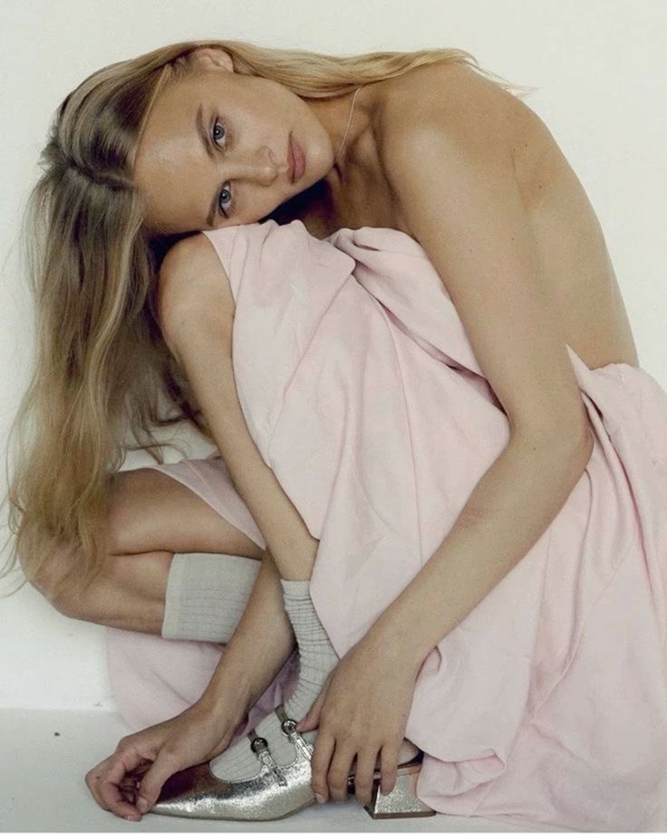Modella con abito rosa e scarpe eleganti in una posa creativa, esprimendo bellezza e stile unico.