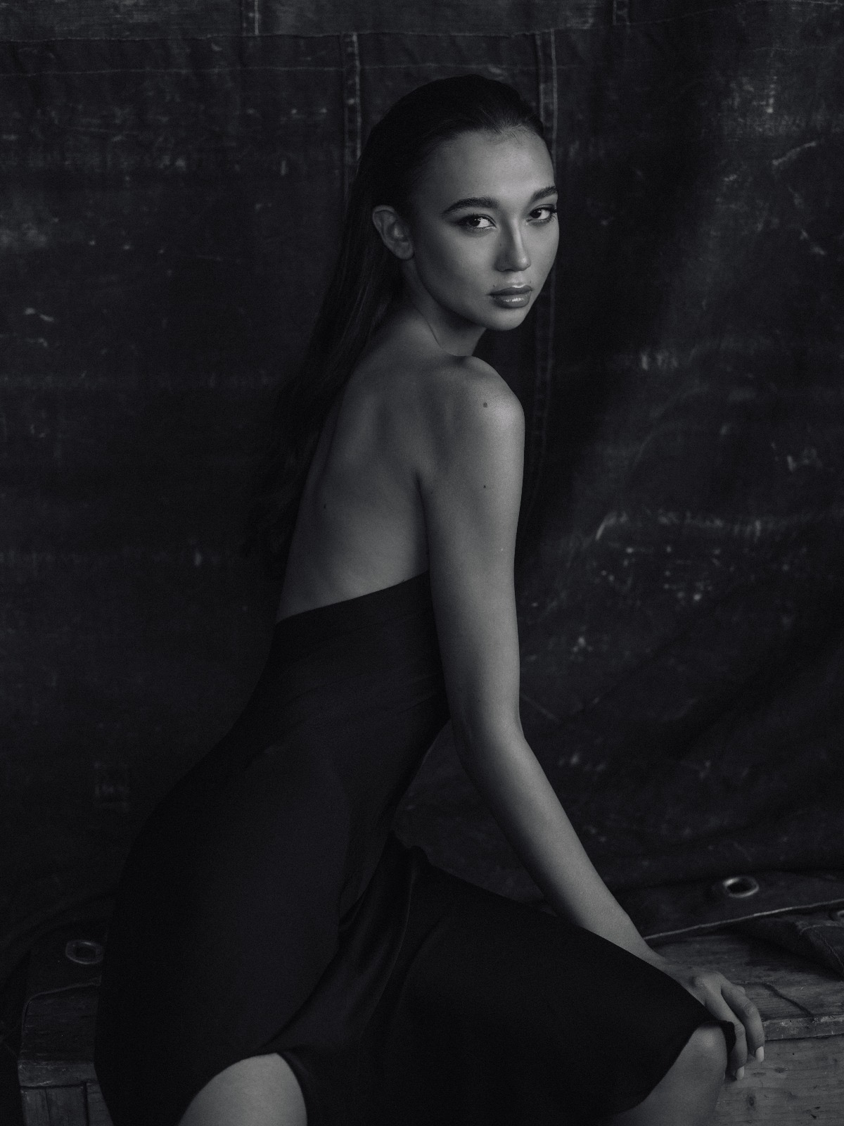 Modella elegante in abito nero, posa raffinata in studio fotografico, bellezza naturale e stile sofisticato.