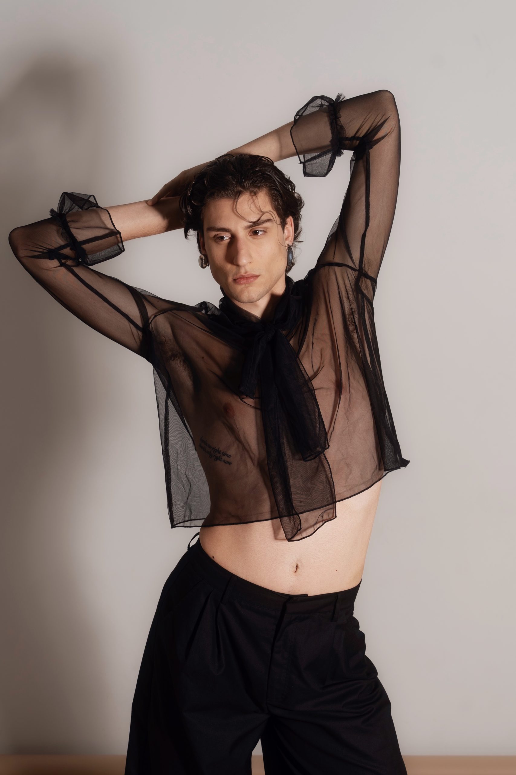 Modello indossa camicia trasparente nera con pantaloni eleganti, tendenze moda alta adatta a Firenze e Milano.