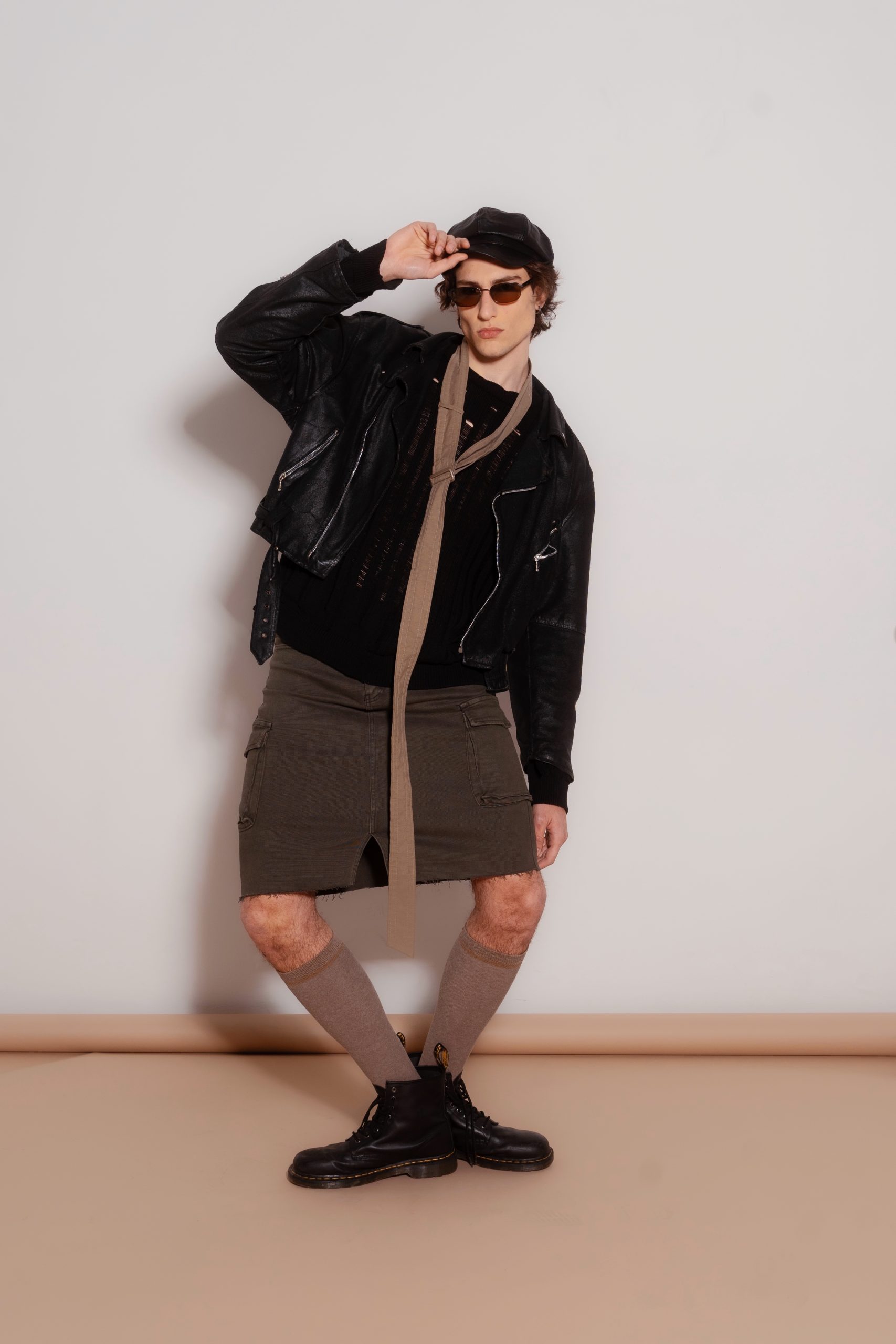 Modello maschile con giacca di pelle, gonna e stivali, look audace e alla moda per sfilate e campagne pubblicitarie.