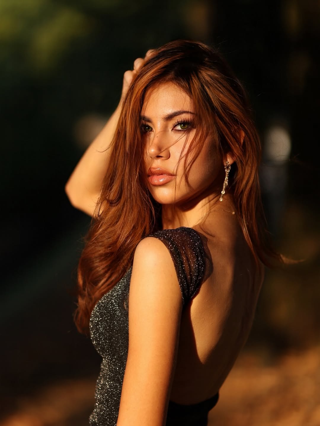 Modella con capelli lunghi e occhi verdi indossa abito scintillante, catturata in un'elegante luce naturale.