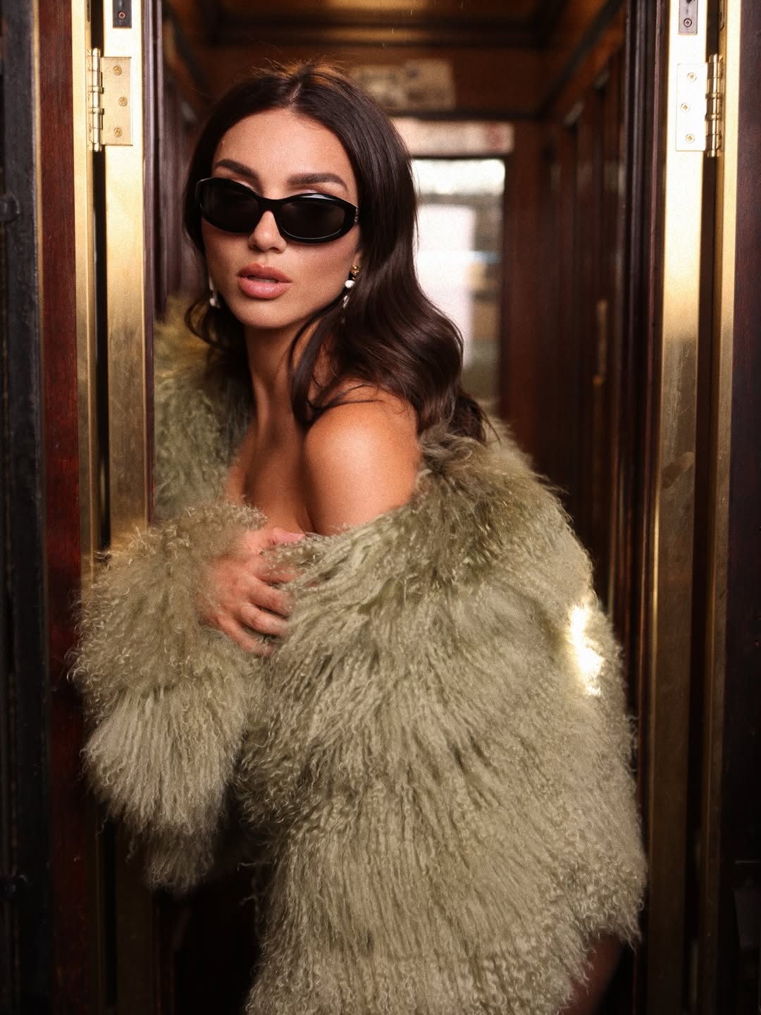 Modella elegante in un cappotto di pelliccia verde, occhiali da sole alla moda, stile raffinato e glamour.