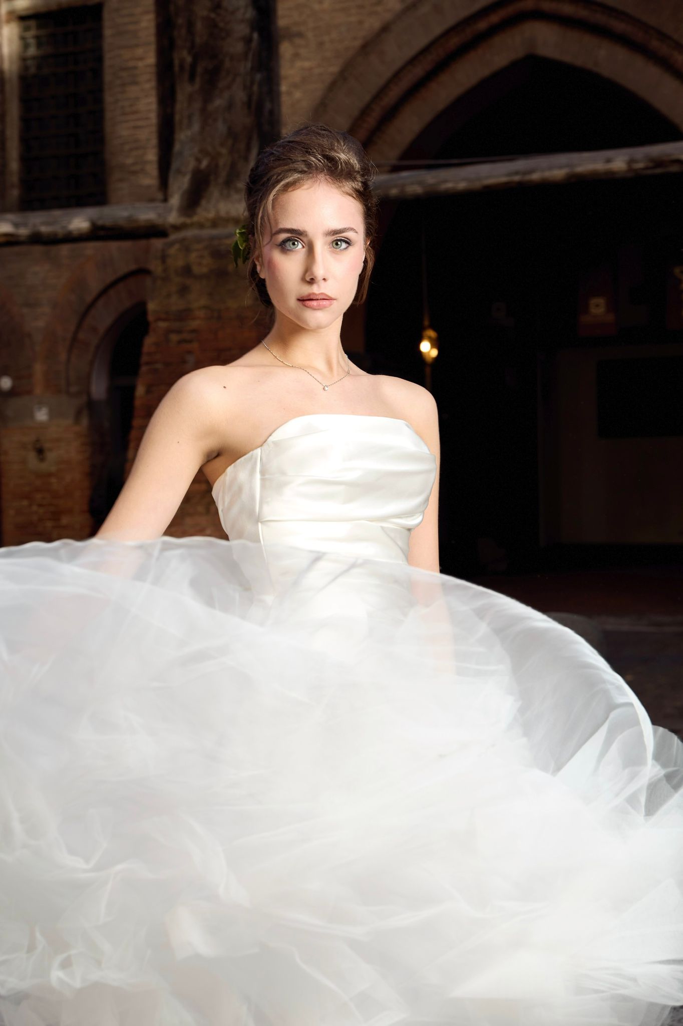 Modella elegante in abito da sposa bianco con volumi setosi e dettagli unici, in una location storica.