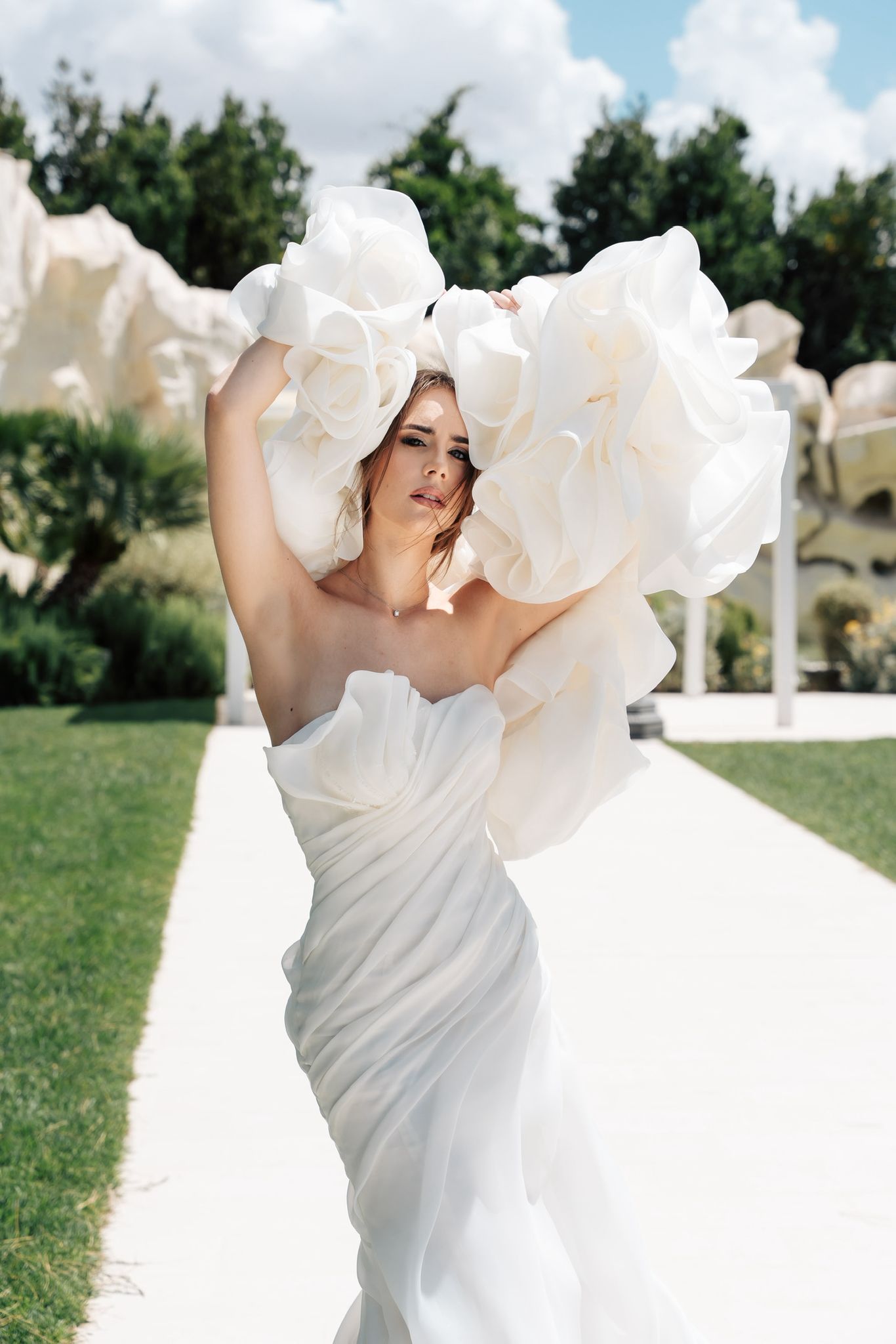 Modella in abito bianco elegante con dettagli floreali, sguardo seducente in un contesto estivo
