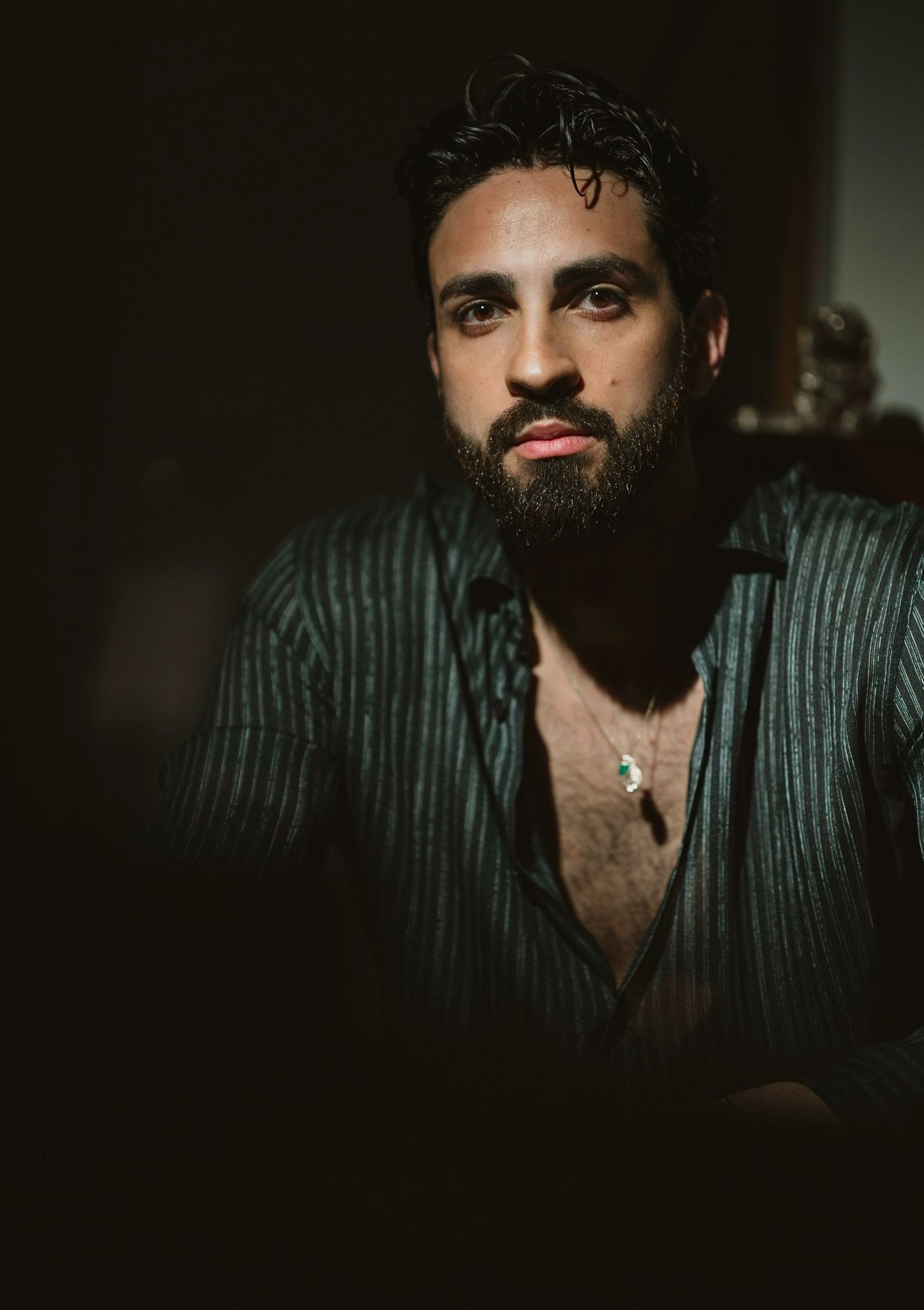 Ritratto di uomo con barba e camicia a strisce, espressione intensa e creazione di atmosfera elegante.