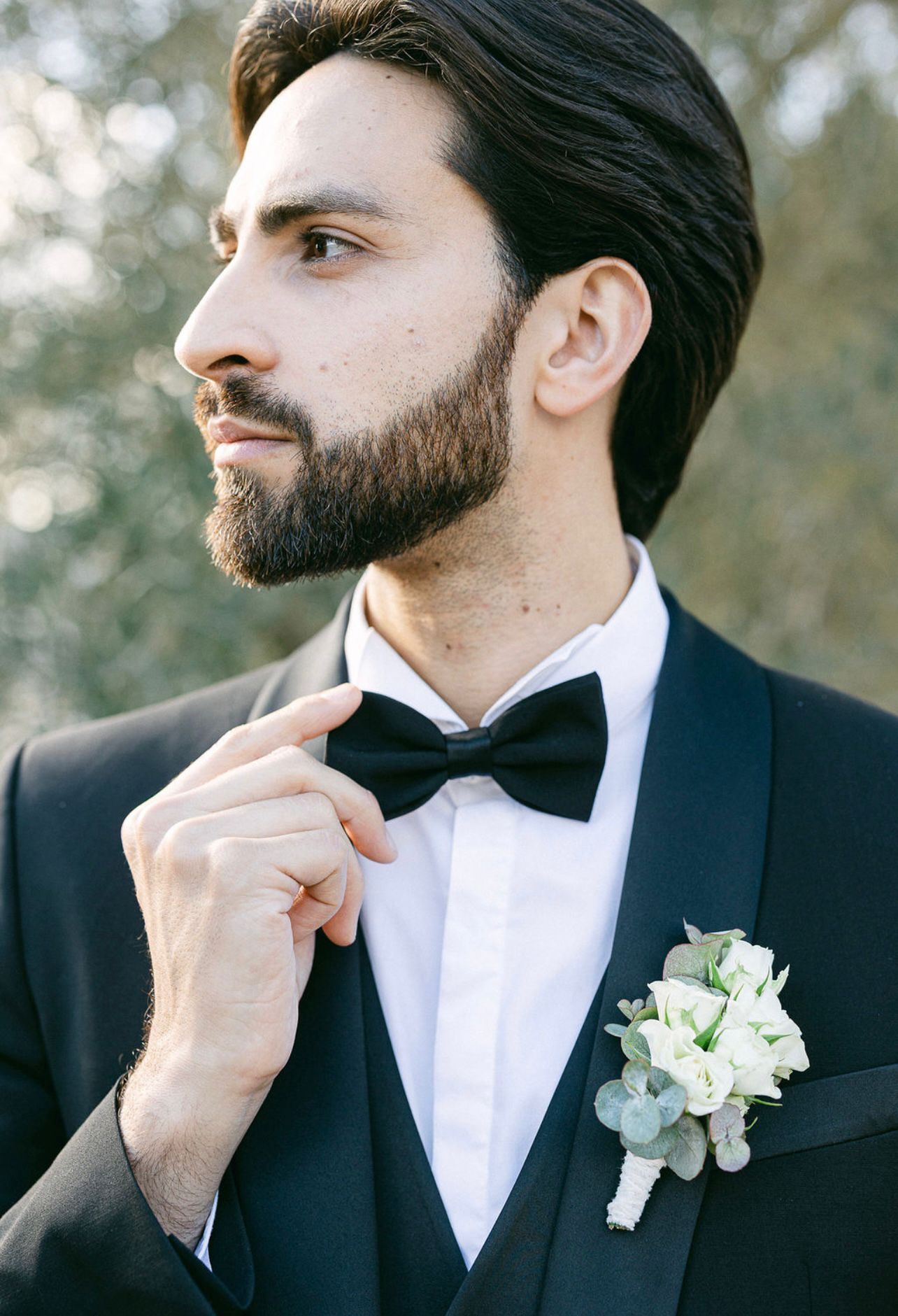 Uomo elegante in abito da cerimonia con papillon e boutonnière, pronto per un evento speciale.