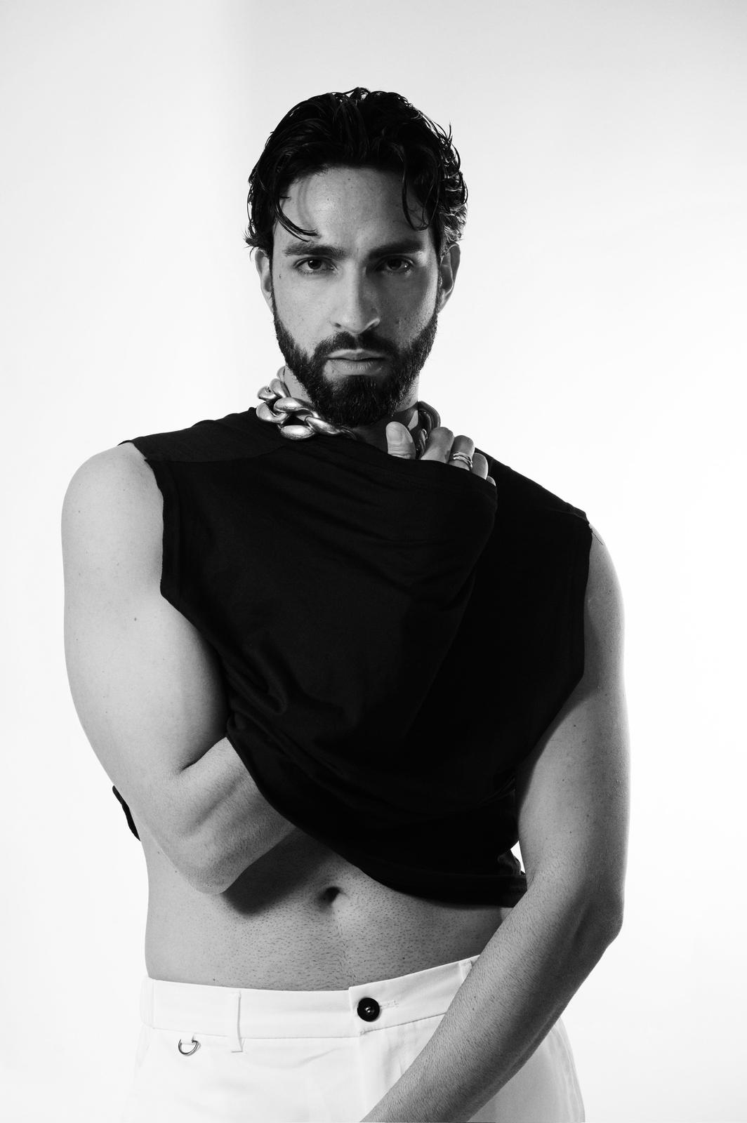 Modello maschile in abbigliamento trendy, ritratto in bianco e nero con collana elegante e sguardo intenso.