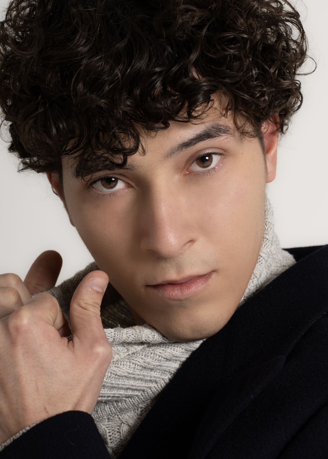 Primo piano di un modello con capelli ricci, indossando un maglione, stile fashion moderno e sofisticato
