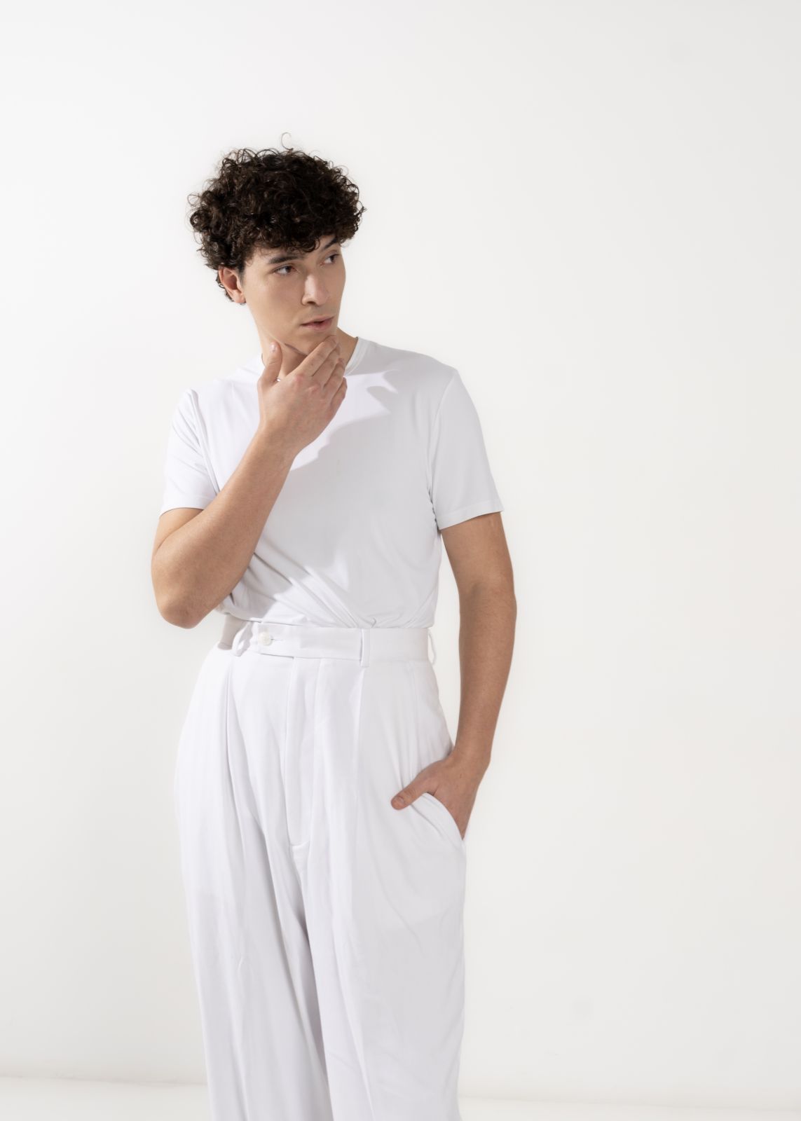 Modello maschile in abbigliamento elegante, t-shirt bianca e pantaloni bianchi, posa raffinata.