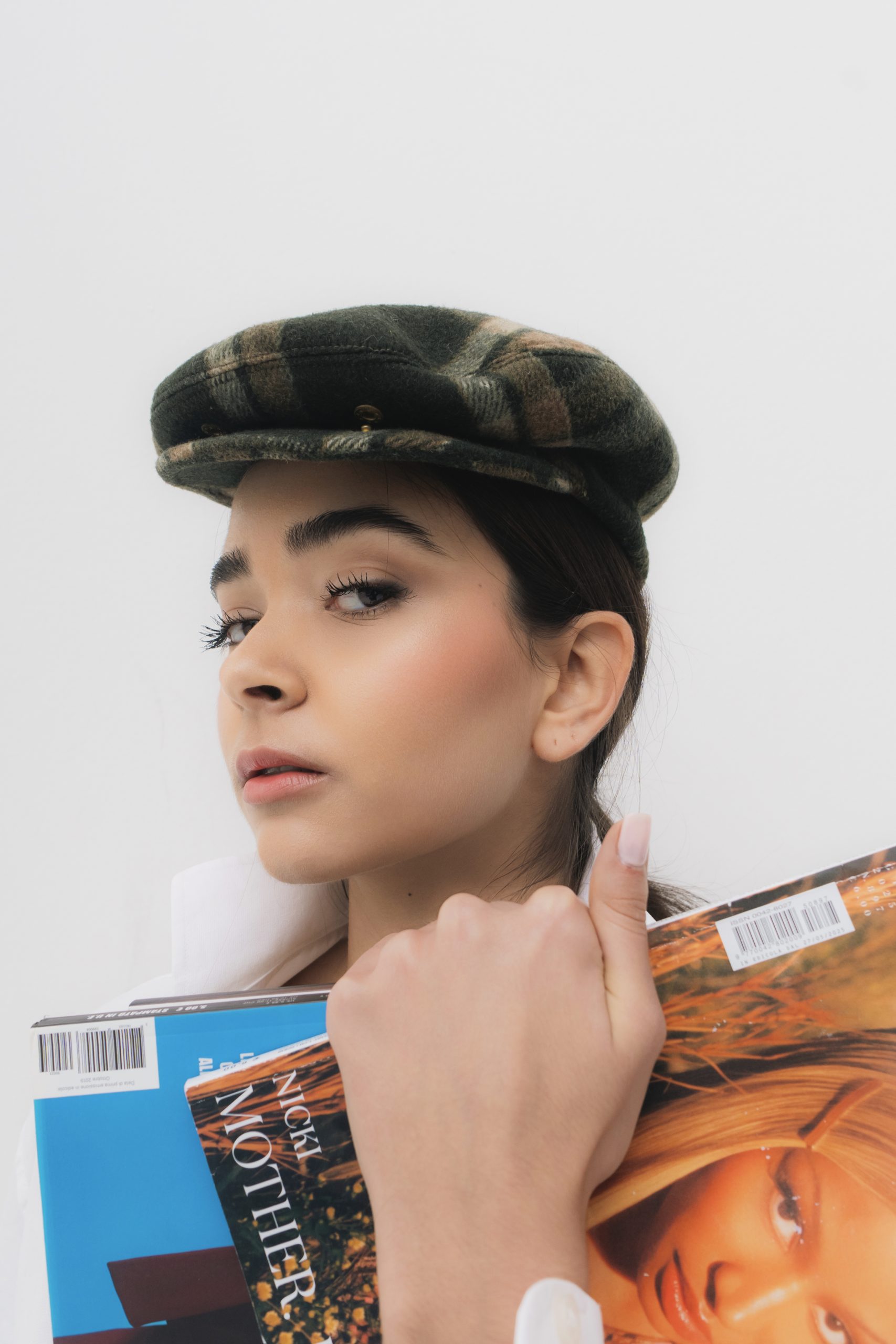 Modella con cappello elegante tiene riviste di moda, rappresenta Fashion Concept Firenze, agenzia di modelli in Italia.