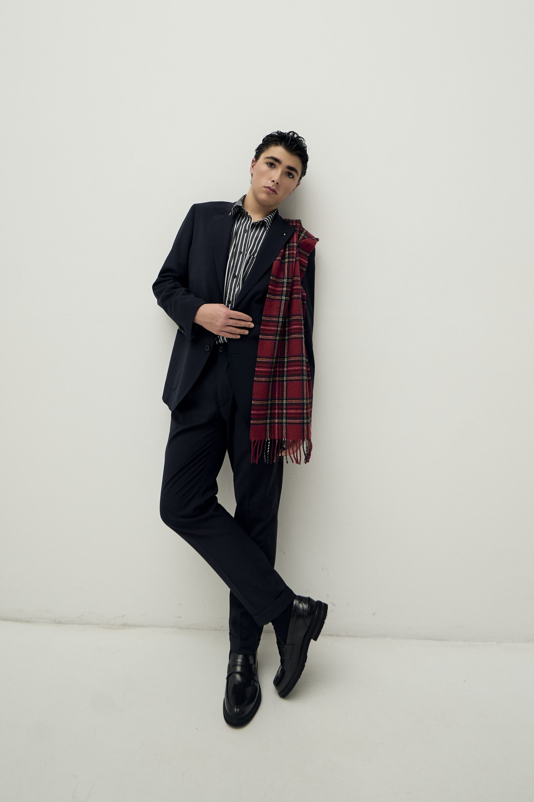 Model giovane in giacca elegante blu con camicia a righe e sciarpa scozzese, stile moda contemporanea.