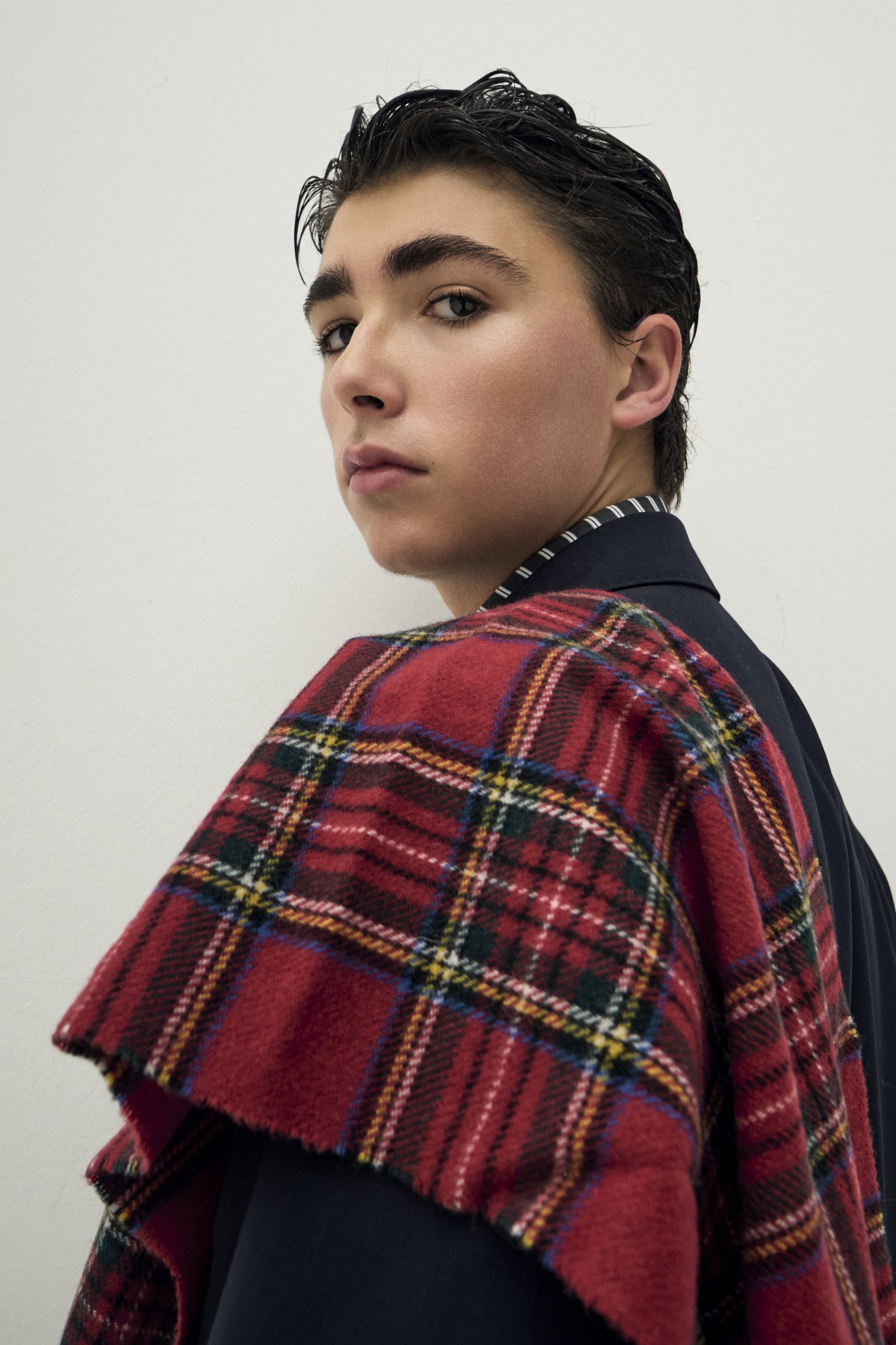 Giovane modello con cappotto scozzese rosso, stile urbano e contemporaneo in un set moda elegante.
