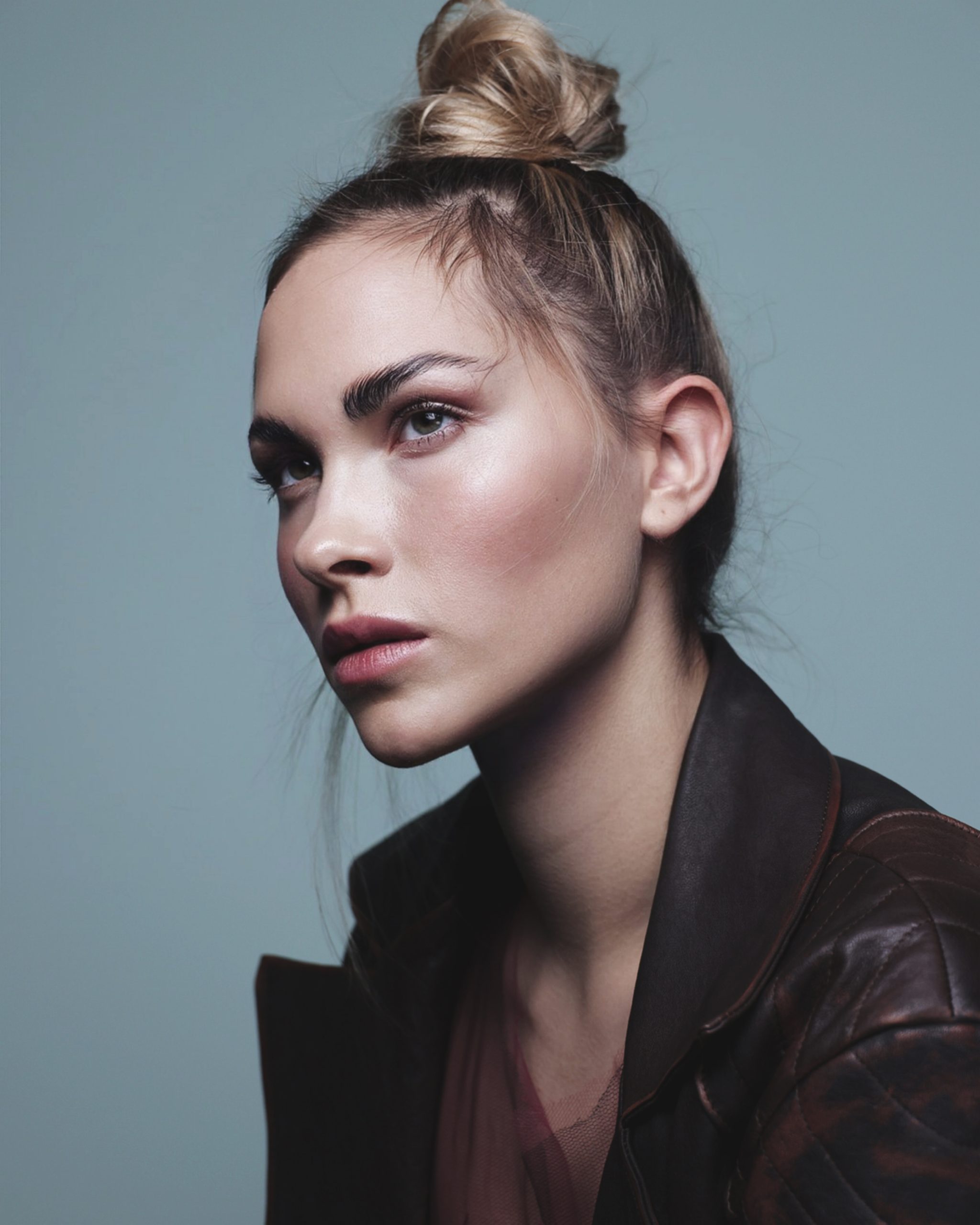 Ritratto elegante di modella con capelli raccolti e giacca in pelle, stile fashion contemporaneo.