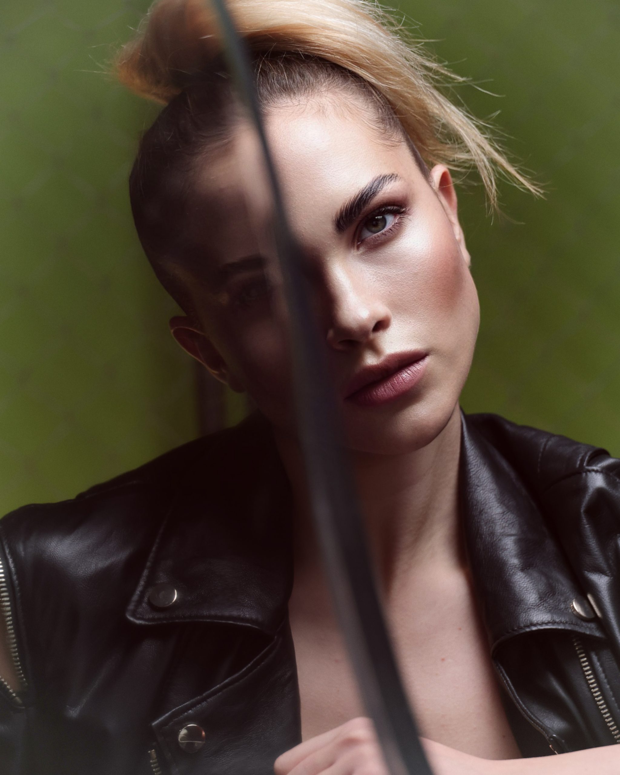Ritratto di modella con giacca di pelle nera, sguardo intenso su sfondo verde, stile fashion moderno