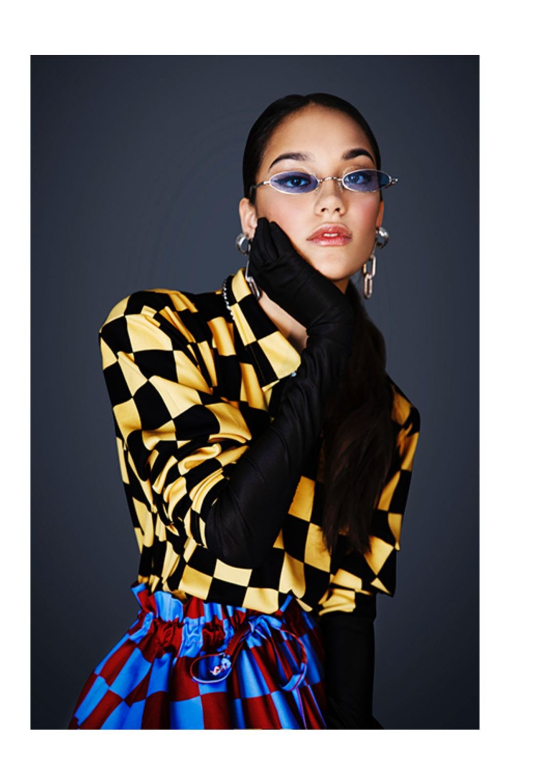 Modella in outfit colorato con camicia a scacchi gialla e gonna a scacchi blu e rossa, accessori fashion eleganti.