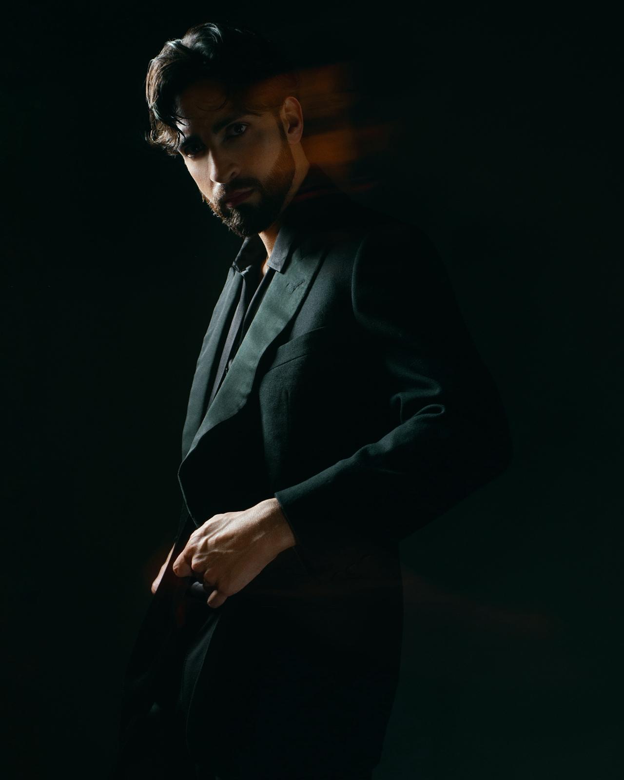 Moderno modello maschile in abito elegante, catturato in scena con atmosfera dark e sofisticata.