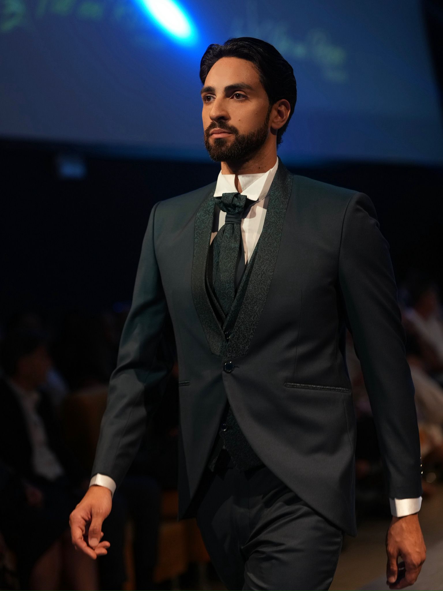 Modello maschile in elegante abito da cerimonia blu, sfilando con stile su passerella fashion.